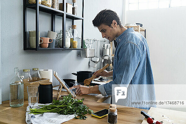 Junger Mann nutzt digitales Tablet beim Zubereiten von Speisen in der Küche