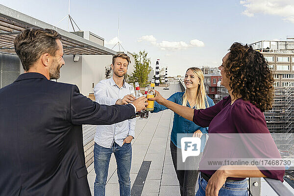 Happy coworkers toasting drink bottles on rooftop