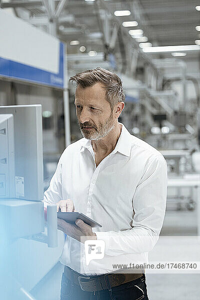 Male professional with digital tablet examining machinery in industry