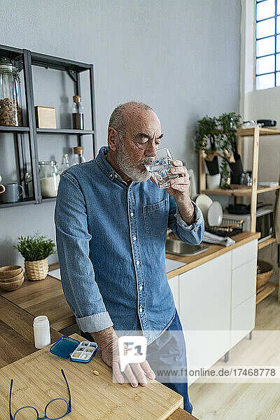 Älterer Mann trinkt Wasser in der heimischen Küche