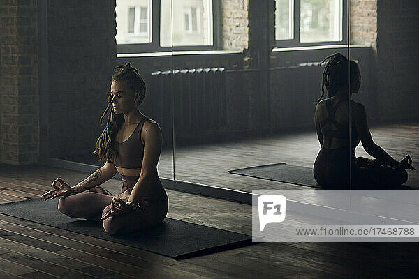 Young woman meditating in front of mirror at yoga studio
