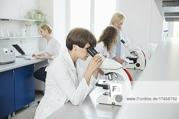 Researcher using microscope with colleagues working in background