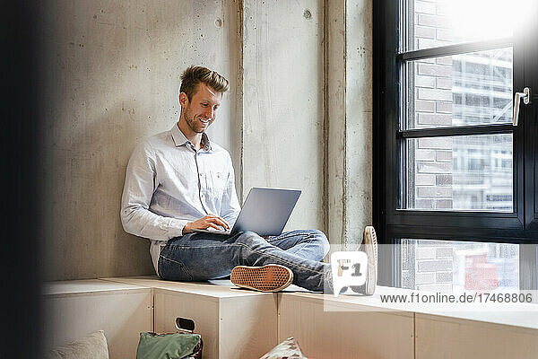 Young businessman using laptop by window in office