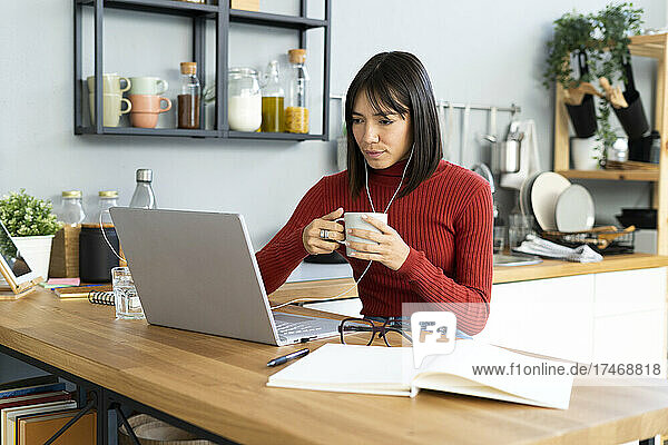 Businesswoman with coffee mug working on laptop at home