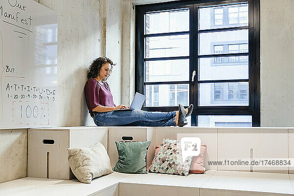 Female entrepreneur using laptop while sitting with legs crossed at ankle in office