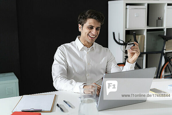 Cheerful businessman doing online shopping through laptop in office