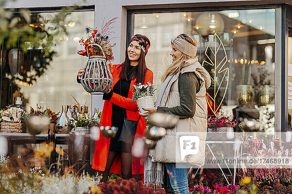 Smiling women holding flower pots in front of shop