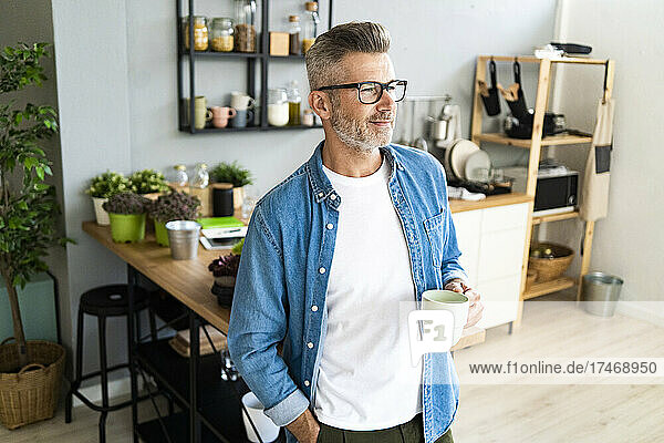 Man with hand in pocket holding coffee cup at home