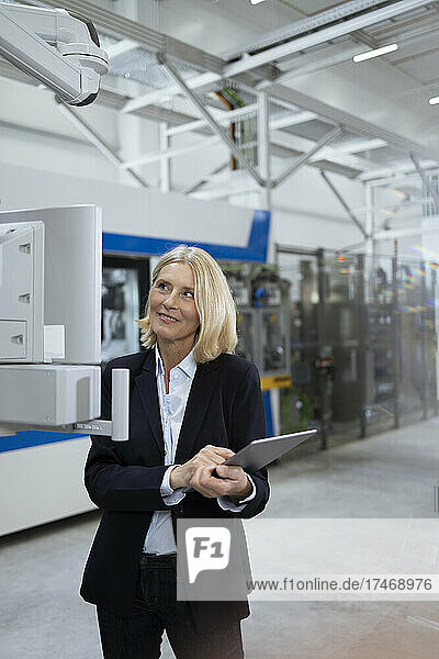 Female professional with digital tablet examining machinery in factory