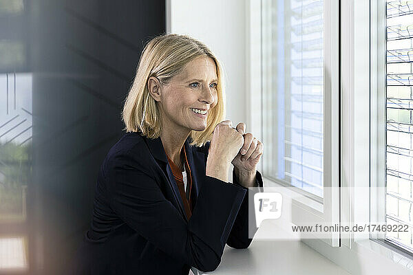 Smiling blond businesswoman looking through window