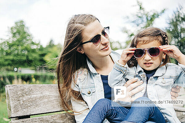 Mother looking at daughter wearing sunglasses while sitting on bench
