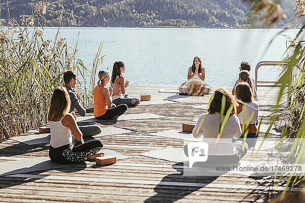 Men and women practicing yoga with instructor on jetty by lake
