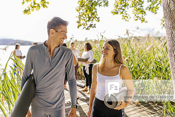 Smiling man and woman looking at each other while holding exercise mats during sunny day