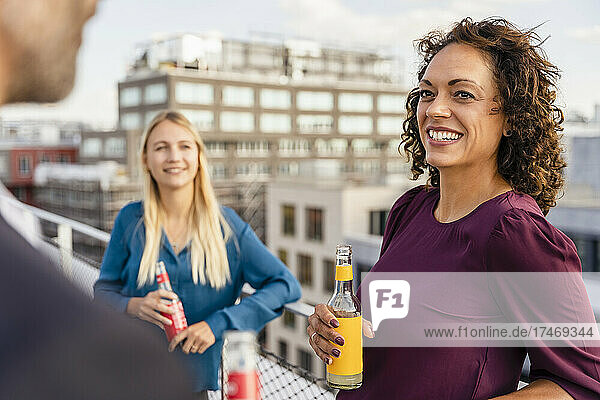 Smiling businesswoman having drink with coworkers on rooftop
