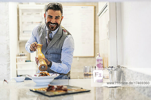 Smiling male chef with pepper grinder at kitchen counter