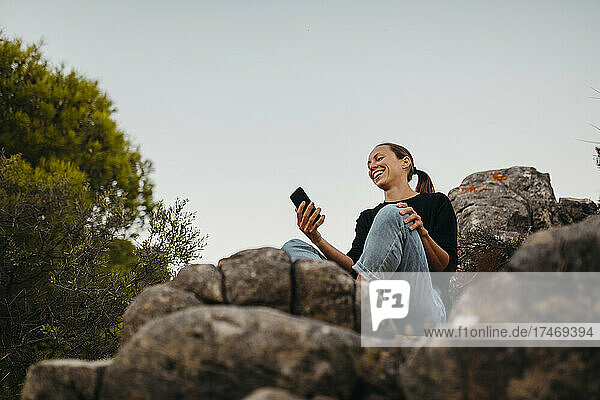 Happy woman using mobile phone on rock