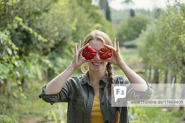 Playful female farmer holding tomatoes in front of eyes