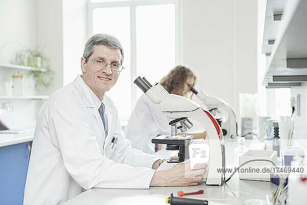 Smiling scientist with microscope in laboratory