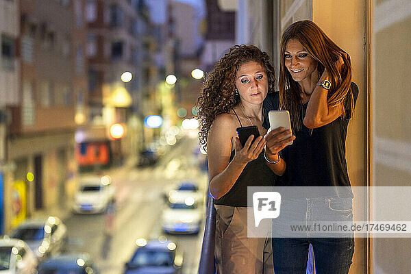 Freundinnen nutzen Smartphones  während sie auf dem Balkon stehen