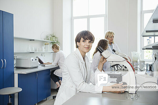 Smiling researcher with microscope at desk