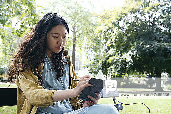 Junge Frau konzentriert sich  während sie im Park Tagebuch schreibt