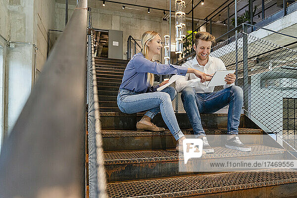 Young coworkers using tablet PC on staircase in office