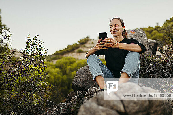 Smiling woman using mobile phone on rock