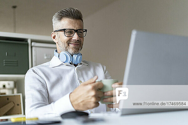 Smiling businessman with coffee mug on video conference through laptop in office