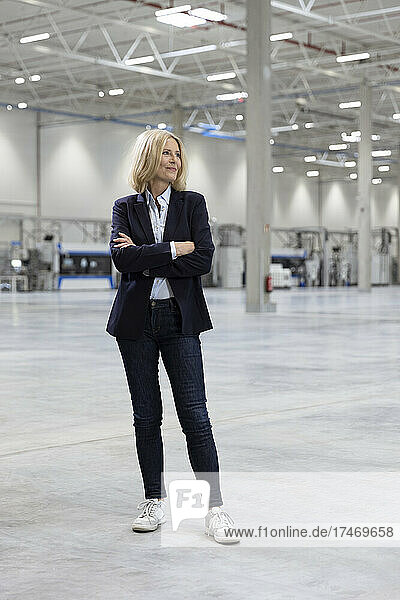 Mature blond businesswoman standing with arms crossed in industry