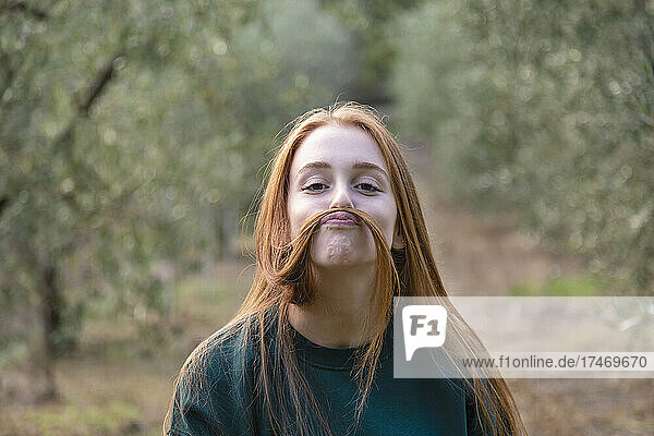 Playful woman making mustache of hair in farm