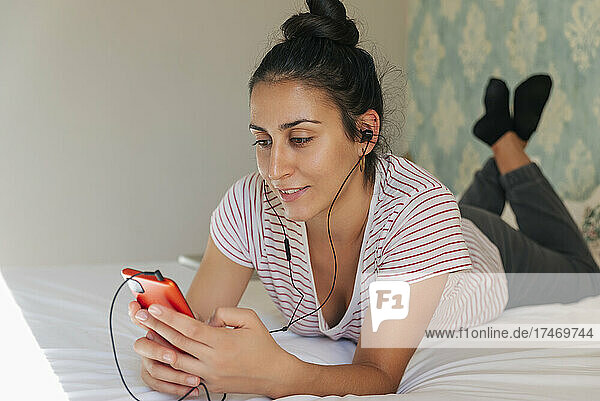 Young woman wearing headphones using smart phone in bedroom