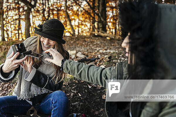 Happy young women taking photographs in autumn forest