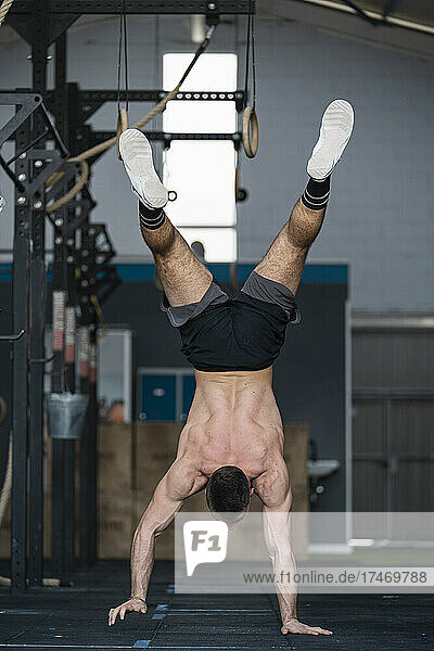 Shirtless sportsman practicing handstand while working out in gym