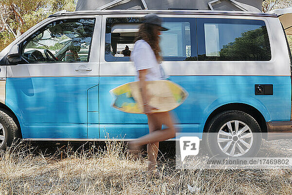 Woman with skateboard walking by camper van
