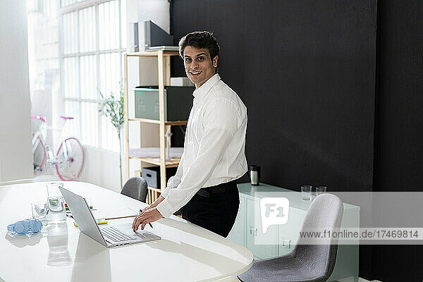 Selbstbewusster Geschäftsmann mit Laptop am Schreibtisch im Büro