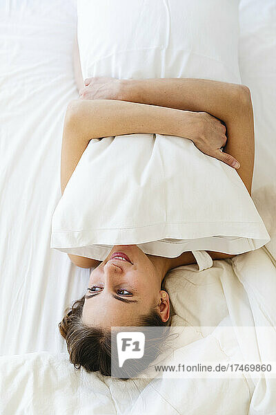 Smiling girl hugging pillow while lying on bed at home