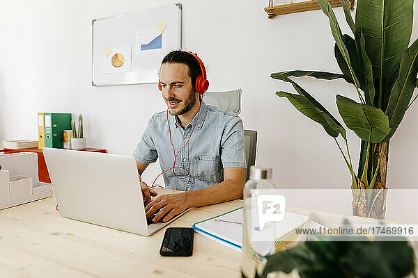 Businessman with headphones using laptop in creative office