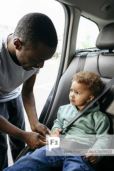 Father adjusting seat belt of daughter sitting in car