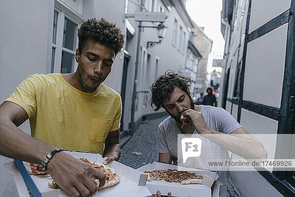 Two friends eating takeaway pizza in the city