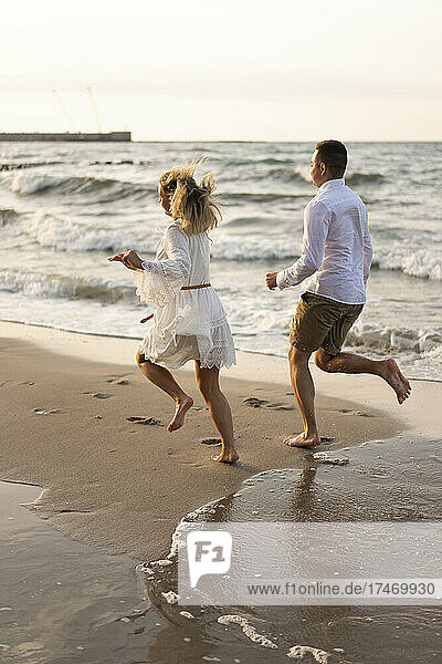 Playful couple running on sand by sea at beach