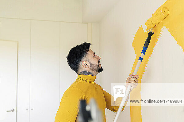 Mid adult man painting wall with paint roller at home