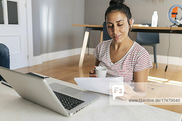 Smiling female freelancer reading document in home office