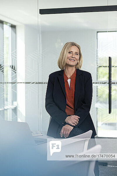 Smiling mature businesswoman sitting on desk in office