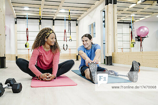 Smiling woman talking with disabled friend exercising in gym