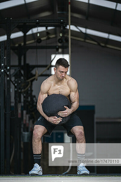 Determined male athlete holding weight bag while exercising in gym