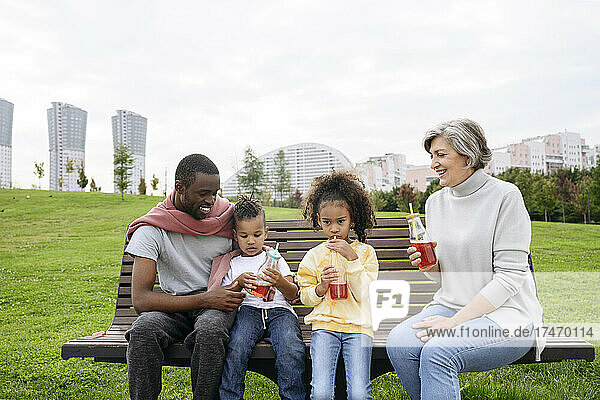 Father looking at children having drink on park bench