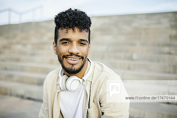 Smiling young man with black curly hair wearing wireless headphones