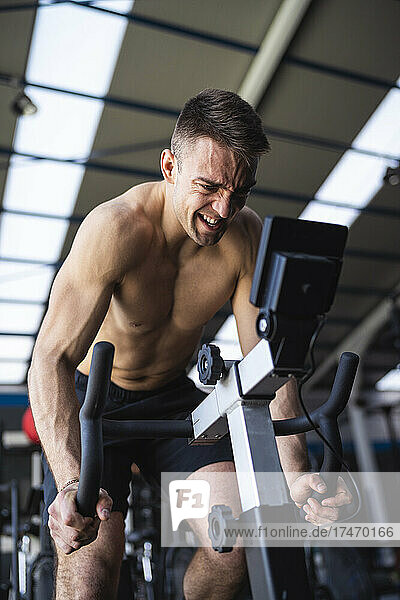 Determined sportsman on exercise bike while working out in gym
