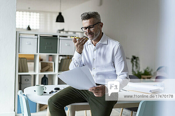 Smiling businessman with documents talking on mobile phone in office