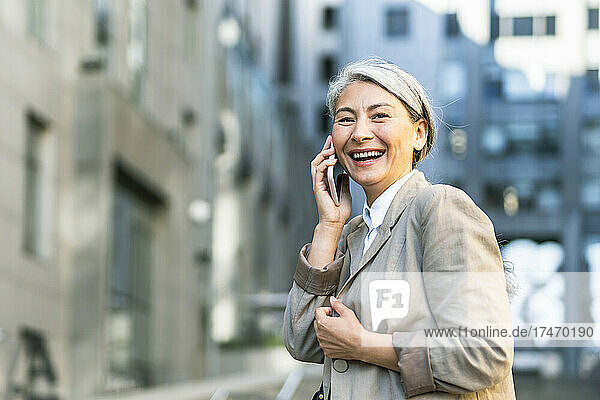 Frau lacht  während sie in der Stadt mit dem Handy telefoniert